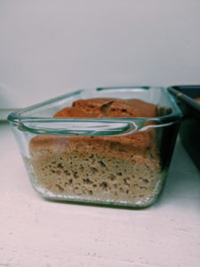 A loaf of sourdough bread in a glass loaf pan, you can see the bubbles in the dough.