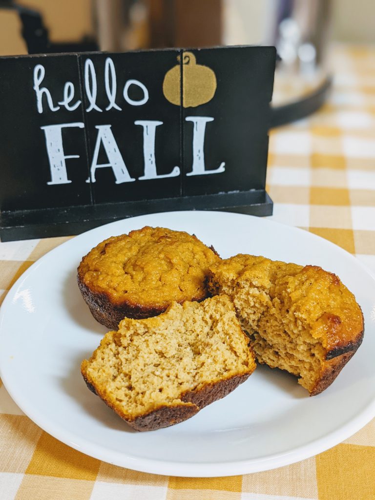 Gluten free pumpkin pie muffins sitting on plate on top of yellow gingham tablecloth.